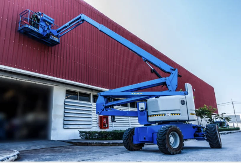 Plataforma articulada azul trabalhando na fachada de um galpão